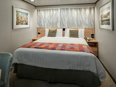 Innenkabine an Bord der Nieuw Amsterdam mit einem großen Bett, bunten Kissen, Nachttischen und gerahmter Kunst an den Wänden.