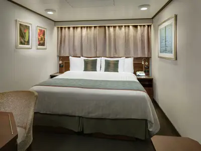 Ein komfortables Doppelbett mit grünem Läufer und dekorativen Kissen in einer modernen Innenkabine an Bord der Nieuw Amsterdam.