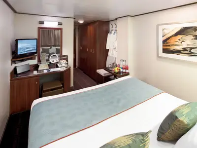 Doppelbett mit hellblauer Decke in einer gemütlich eingerichteten Innenkabine an Bord der Nieuw Amsterdam.