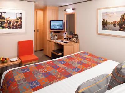 Blick in eine gemütliche Innenkabine an Bord der Nieuw Amsterdam mit Doppelbett, orangefarbenem Sessel und Schreibtisch.