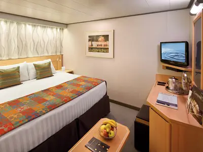 Eine gemütlich eingerichtete Innenkabine an Bord der Nieuw Amsterdam mit einem großen Doppelbett, Schreibtisch und Fernseher.