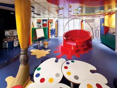 Der bunte Kinderbereich an Bord der Nieuw Amsterdam mit einem riesigen Pinsel, Tischen in Palettenform und rotem Sofa.
