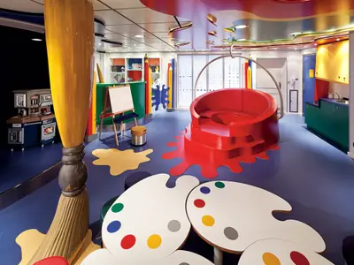 Bunter Club HAL Kinderbereich an Bord der Nieuw Amsterdam mit riesigem Pinsel, Tischen in Palettenform und einer roten Spielecke.