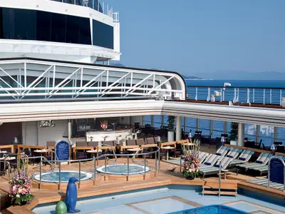 Blick auf das sonnige Lido-Pooldeck an Bord der Nieuw Amsterdam mit Whirlpools, Liegen und Meerblick.