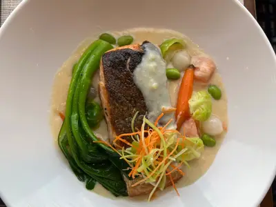 Ein auf einem Teller kunstvoll angerichtetes Lachsgericht mit Gemüse an Bord der Nieuw Amsterdam im Restaurant Morimoto By Sea.