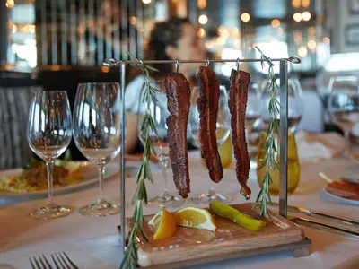 Kandierter Speck, der an einem Gestell mit Rosmarin serviert wird, im Pinnacle Grill an Bord der Nieuw Amsterdam.