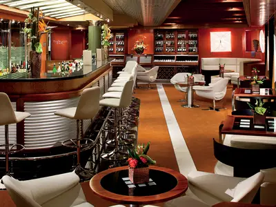 Die stilvolle Pinnacle Bar an Bord der Nieuw Amsterdam mit weißen Barhockern, Sesseln und einer edlen Holztheke.