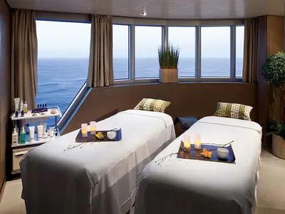 Zwei Massageliegen mit Dekoration in einem hellen Behandlungsraum mit Meerblick an Bord der Nieuw Amsterdam.