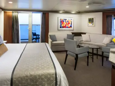 Blick in eine luxuriöse Neptune Spa Suite an Bord der Nieuw Amsterdam mit Kingsize-Bett, Sitzbereich und Zugang zum Balkon.