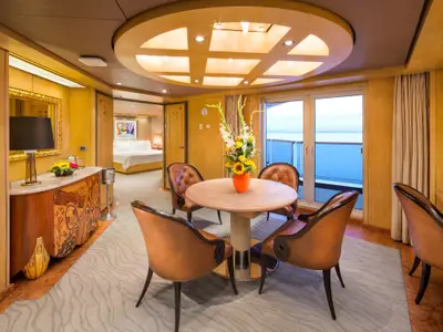 Blick in die elegante Pinnacle Suite an Bord der Nieuw Amsterdam mit rundem Holztisch, Ledersesseln und Balkon mit Meerblick.