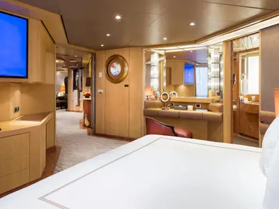 Einblick in eine großzügige Suite an Bord der Nieuw Amsterdam mit Doppelbett, Frisiertisch, Spiegel und edler Holztäfelung.