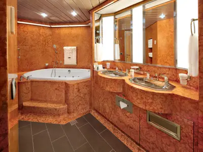 Das luxuriöse Badezimmer einer Suite an Bord der Nieuw Amsterdam mit rötlichem Marmor, Whirlpool-Badewanne und zwei Waschbecken.