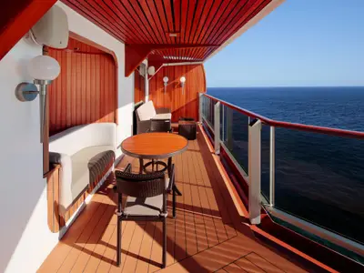 Balkon der Pinnacle Suite an Bord der Nieuw Amsterdam mit Holzverkleidung, Sitzmöbeln und Blick auf das blaue Meer.