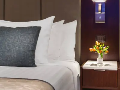 Detailansicht eines gemachten Betts mit Kissen und Blumen auf dem Nachttisch in einer Suite an Bord der Nieuw Amsterdam.