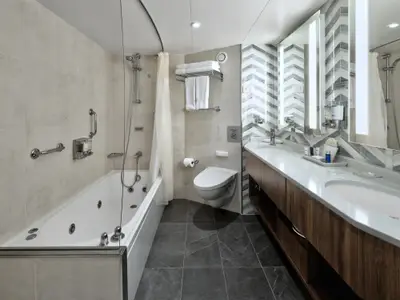 Das helle und luxuriöse Badezimmer einer Neptune Suite mit Doppelwaschbecken und Whirlpool-Badewanne an Bord der Nieuw Amsterdam.