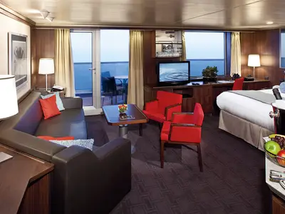 Luxuriöse Suite an Bord der Nieuw Amsterdam mit braunem Ledersofa, roten Sesseln, Balkon und einem großen Bett.