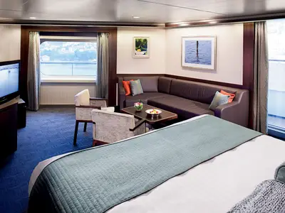 Luxuriöse Neptune Suite an Bord der Nieuw Amsterdam mit einem großen Bett, einer Couch, Sesseln und Balkonzugang.