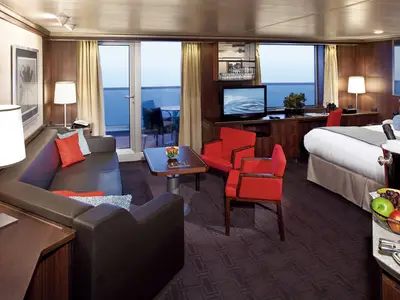 Luxuriöse Neptune Suite an Bord der Nieuw Amsterdam mit Couch, zwei roten Sesseln, Doppelbett und Balkon-Ausblick aufs Meer.