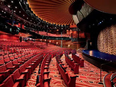 Blick in das elegante Theater an Bord der Nieuw Amsterdam mit roten Sitzen, einer dunklen Bühne und goldenem Vorhang.