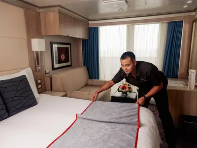 Ein Kabinensteward richtet sorgfältig das Bett in einer modernen Balkonkabine an Bord der Nieuw Statendam her.
