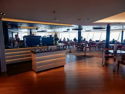 Blick in die stilvoll beleuchtete Crow's Nest Lounge an Bord der Nieuw Statendam mit gemütlichen Sitzgruppen und großen Panoramafenstern.