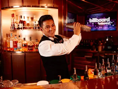 Ein Barkeeper im eleganten Gewand bereitet an der Billboard Bar an Bord der Nieuw Statendam einen Cocktail zu.