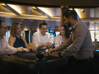 Eine Gruppe von Gästen spielt an Bord der Nieuw Statendam an einem Spieltisch im Casino, während ein Croupier Karten verteilt.