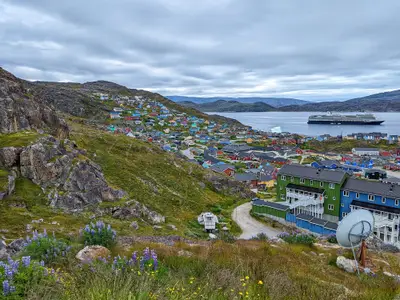 Blick über grüne Hügel und bunte Häuser in Qaqortoq auf die im Fjord liegende Nieuw Statendam.
