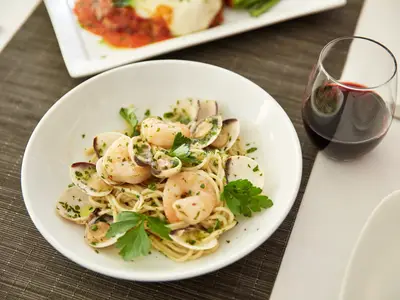 Ein Teller frische Pasta mit Garnelen und Muscheln neben einem Glas Rotwein an Bord der Nieuw Statendam im Canaletto Restaurant.