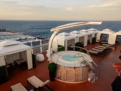 Exklusiver Entspannungsbereich "The Retreat" an Bord der Nieuw Statendam mit Whirlpool, privaten Cabanas und Sonnenliegen auf dem Holzdeck vor dem Meer.