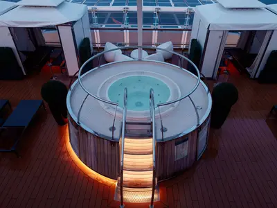 Ein beleuchteter runder Whirlpool mit Holzverkleidung und Treppe im Retreat-Bereich an Bord der Nieuw Statendam.