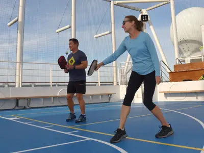 Ein Mann und eine Frau spielen Pickleball auf dem blauen Sportplatz auf dem Außendeck an Bord der Nieuw Statendam.