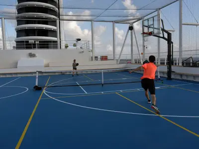 Zwei Personen beim aktiven Pickleball-Spiel auf dem blauen Sportplatz-Außendeck an Bord der Nieuw Statendam.