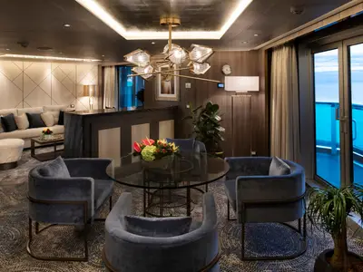 Blick in die luxuriöse Suite an Bord der Nieuw Statendam mit runden Samtsesseln, Glastisch und Balkon mit Meerblick.