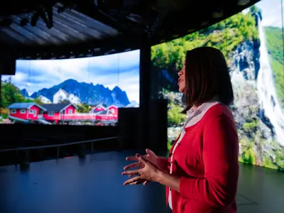 Eine Frau in Rot präsentiert auf der World Stage an Bord der Nieuw Statendam vor einer riesigen, gebogenen LED-Wand mit Landschaftsbildern.