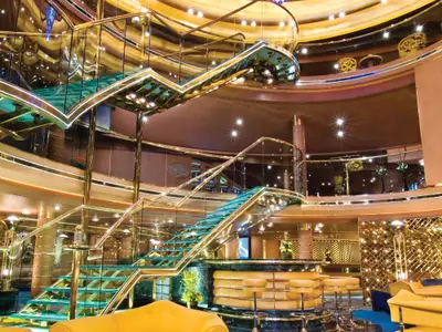 Blick auf die geschwungene Glastreppe und das elegante Atrium an Bord der Noordam mit warmer Beleuchtung.