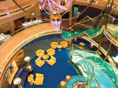 Blick von oben in das Atrium an Bord der Noordam mit geschwungener Glastreppe und gelben Sesseln auf blauem Teppich.