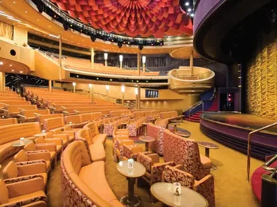 Blick in die prächtige Vista Lounge an Bord der Noordam mit gelben Sesselreihen, goldener Bühne und roter Decke.