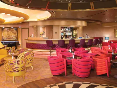 Die stilvolle Ocean Bar an Bord der Noordam bietet rote Sessel, goldene Verzierungen und eine geschwungene Bartheke in warmer Atmosphäre.