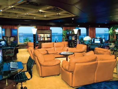 Innenansicht des Explorations Café an Bord der Noordam mit orangefarbenen Ledersesseln, Computern und Meerblick.
