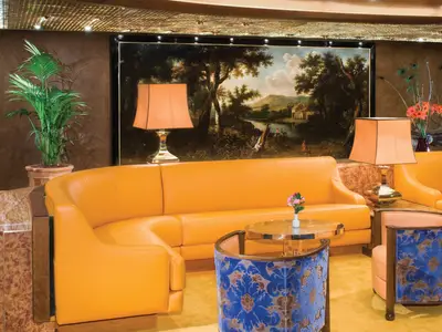 Die Explorer's Lounge an Bord der Noordam zeigt ein orangefarbenes Ledersofa, blaue Sessel und ein klassisches Landschaftsgemälde.