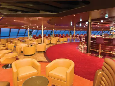 Die großzügige Crow's Nest Lounge an Bord der Noordam mit gelben Ledersesseln, rotem Teppich, einer Bar und Meerblick durch die Fensterfront.