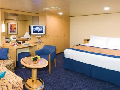 Blick in eine gemütlich eingerichtete Innenkabine an Bord der Noordam mit einem Doppelbett, blauem Sessel und Holzmöbeln.