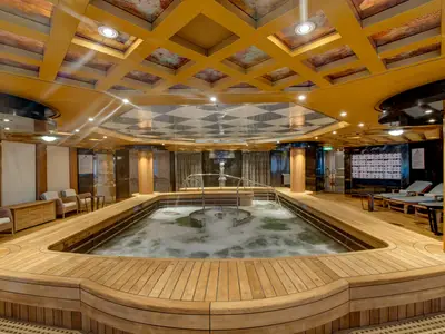 Blick auf den großzügigen, sprudelnden Hydrotherapie-Pool im Wellnessbereich an Bord der Noordam mit Holzdeck und Liegen.