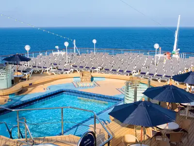 Blick auf den Sea View Pool an Bord der Noordam mit blau-weißen Liegestühlen und Sonnenschirmen unter klarem Himmel.