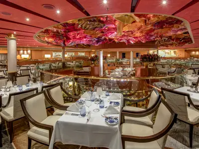 Elegantes Restaurant an Bord der Noordam mit weiß gedeckten Tischen und einer farbenfrohen Deckeninstallation.