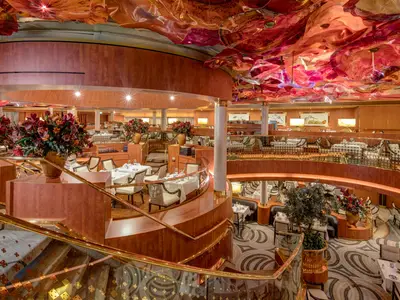 Der stilvolle Hauptspeisesaal an Bord der Noordam zeigt elegant gedeckte Tische, geschwungene Treppen und eine rote Decken-Kunstinstallation.