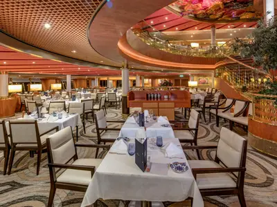 Der elegant eingerichtete Hauptspeisesaal an Bord der Noordam mit gedeckten Tischen und einer geschwungenen Treppe.