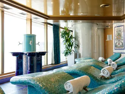 Die elegante Thermal-Suite an Bord der Noordam zeigt beheizte Liegen mit Mosaikfliesen, weiße Handtücher und einen blauen Trinkbrunnen.