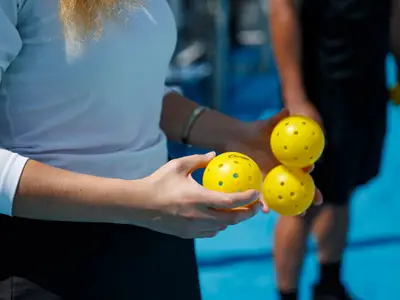 Zwei Personen halten gelbe Picklebälle auf dem blauen Sportplatz an Bord der Noordam an einem sonnigen Tag.